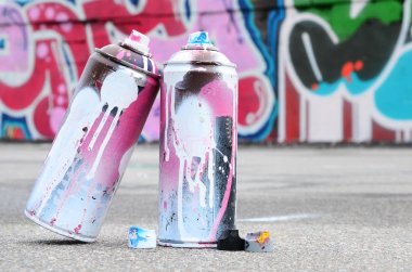 Pembe ve beyaz boya ve baskı altında boya püskürtme için kapaklar ile çeşitli kullanılan sprey kutular renkli grafiti çizimler boyalı duvarın yanında asfalt üzerinde yalan olduğunu
