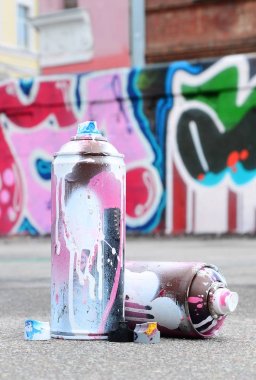 Pembe ve beyaz boya ve baskı altında boya püskürtme için kapaklar ile çeşitli kullanılan sprey kutular renkli grafiti çizimler boyalı duvarın yanında asfalt üzerinde yalan olduğunu