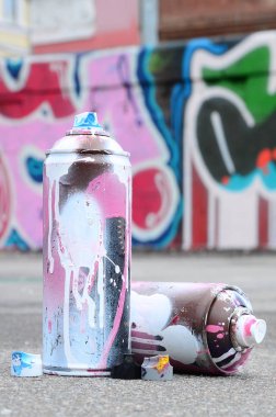 Pembe ve beyaz boya ve baskı altında boya püskürtme için kapaklar ile çeşitli kullanılan sprey kutular renkli grafiti çizimler boyalı duvarın yanında asfalt üzerinde yalan olduğunu