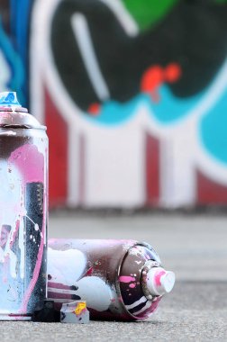 Pembe ve beyaz boya ve baskı altında boya püskürtme için kapaklar ile çeşitli kullanılan sprey kutular renkli grafiti çizimler boyalı duvarın yanında asfalt üzerinde yalan olduğunu