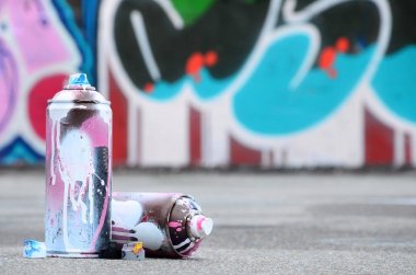 Pembe ve beyaz boya ve baskı altında boya püskürtme için kapaklar ile çeşitli kullanılan sprey kutular renkli grafiti çizimler boyalı duvarın yanında asfalt üzerinde yalan olduğunu