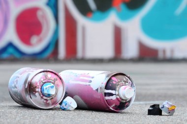 Pembe ve beyaz boya ve baskı altında boya püskürtme için kapaklar ile çeşitli kullanılan sprey kutular renkli grafiti çizimler boyalı duvarın yanında asfalt üzerinde yalan olduğunu