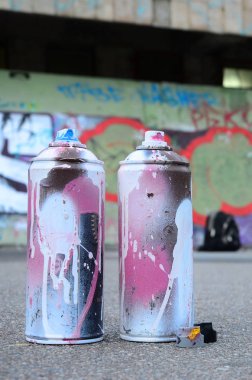 Pembe ve beyaz boya ve baskı altında boya püskürtme için kapaklar ile çeşitli kullanılan sprey kutular renkli grafiti çizimler boyalı duvarın yanında asfalt üzerinde yalan olduğunu