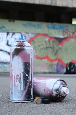 Pembe ve beyaz boya ve baskı altında boya püskürtme için kapaklar ile çeşitli kullanılan sprey kutular renkli grafiti çizimler boyalı duvarın yanında asfalt üzerinde yalan olduğunu
