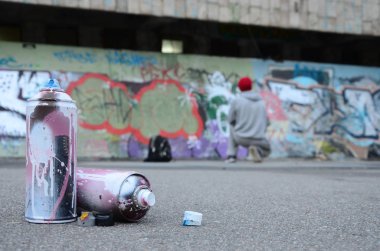 Birkaç kullanılan sprey pembe ve beyaz boya ile renkli grafiti bir boyalı duvar önünde duran adam asfaltta çizimler yalan