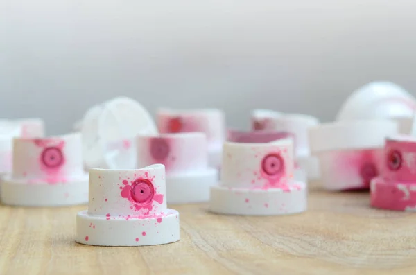 Several plastic nozzles from a paint sprayer that lie on a wooden surface against a gray wall background. The caps are smeared in pink paint. The concept of street art and graffiti