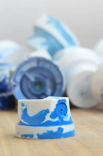 Several plastic nozzles from a paint sprayer that lie on a wooden surface against a gray wall background. The caps are smeared in blue paint. The concept of street art and graffiti