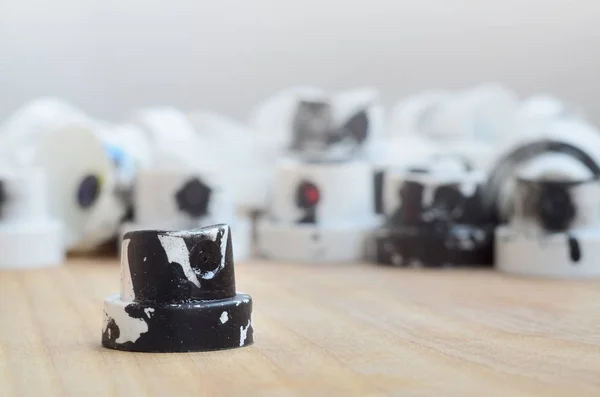 Several plastic nozzles from a paint sprayer that lie on a wooden surface against a gray wall background. The caps are smeared in black paint. The concept of street art and graffiti