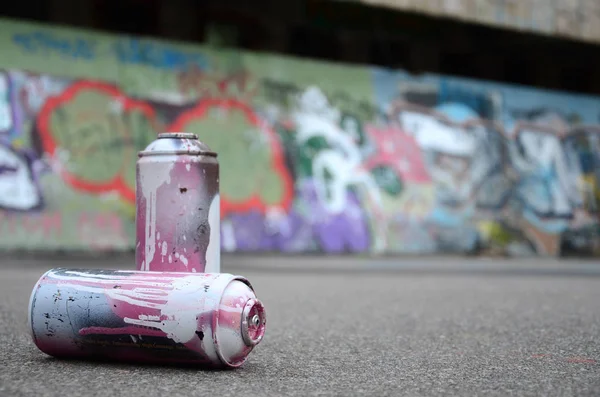 Birkaç kullanılan sprey kutular pembe ve beyaz boya ile renkli grafiti çizimlerinde boyalı duvar arka planı asfalt üzerinde yalan