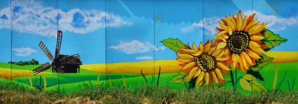 The old wall, painted in color graffiti drawing with aerosol paints. An image of a traditional Ukrainian landscape with sunflowers, kalina and a mill in a field