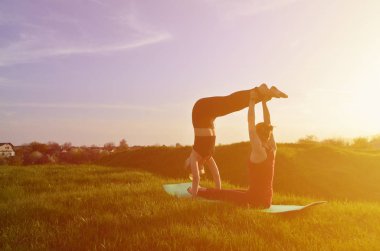İki genç sarışın kız spor pratik yoga açık havada pitoresk bir yeşil tepenin üzerinde akşam uygun. Açık havada spor egzersiz kavramı