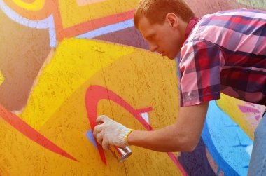 Bir genç Kızıl saçlı grafiti sanatçısı yeni bir graffiti duvar boyar. Bir duvara yakın çekim bir grafiti çizim işlemi fotoğrafı. Sokak sanatı ve yasadışı vandalizm kavramı
