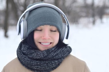 Oldukça çekici beyaz gözlü kız hipster kış park portresi. Kulaklıklar üzerinde müzik dinliyor. Gençlik sokak moda. Kış eğlence.