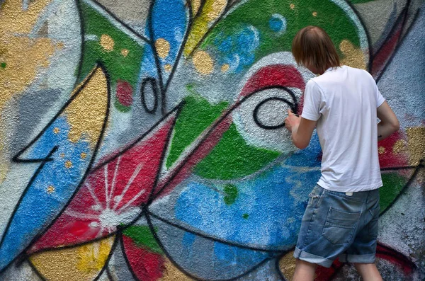 在旧的混凝土墙上画涂鸦图案的过程中的照片 年轻的长发金发男人画了一幅不同颜色的抽象图画 街头艺术与破坏概念 — 图库照片