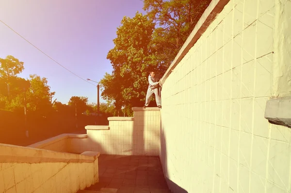 A young guy overcomes obstacles, climbing on concrete walls. The athlete practices parkour, training in street conditions. The concept of sports subcultures among youth