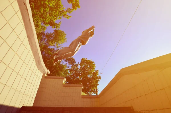 A young guy performs a jump through the space between the concrete parapets. The athlete practices parkour, training in street conditions. Bottom view