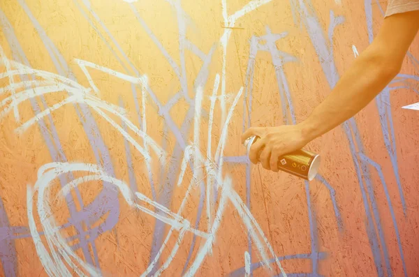 A hand with a spray can that draws a new graffiti on the wall. Photo of the process of drawing a graffiti on a wooden wall close-up. The concept of street art and illegal vandalism