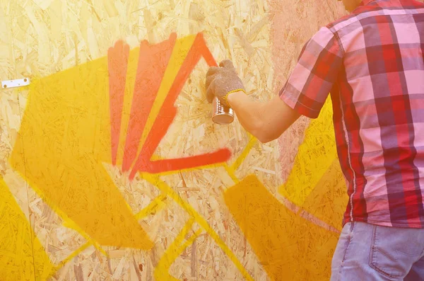 A hand with a spray can that draws a new graffiti on the wall. Photo of the process of drawing a graffiti on a wooden wall close-up. The concept of street art and illegal vandalism