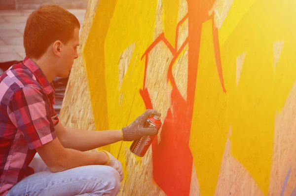 A young red-haired graffiti artist paints a new graffiti on the wall. Photo of the process of drawing a graffiti on a wall close-up. The concept of street art and illegal vandalism