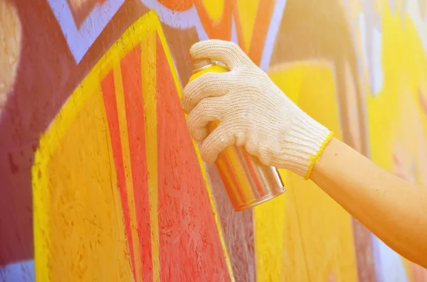 A hand with a spray can that draws a new graffiti on the wall. Photo of the process of drawing a graffiti on a wooden wall close-up. The concept of street art and illegal vandalism