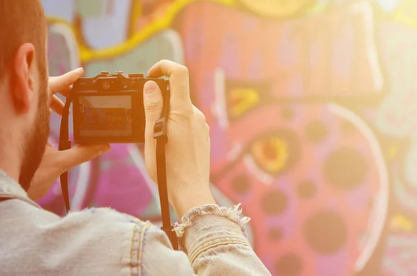 A young graffiti artist photographs his completed picture on the wall. The guy uses modern technology to capture a colorful abstract graffiti drawing. Focus on the photographing device