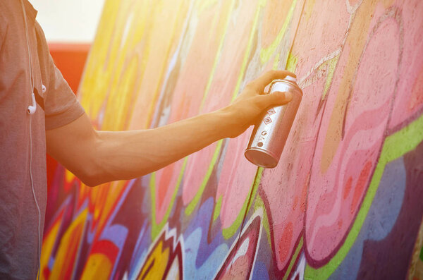 A young red-haired graffiti artist paints a new graffiti on the wall. Photo of the process of drawing a graffiti on a wall close-up. The concept of street art and illegal vandalism