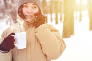 Oldukça çekici beyaz gözlü kız hipster kış Park portresi. Modern smartphone ve içecek kahve konuşuyor. Gençlik sokak moda. Açık havada yürüyüşler