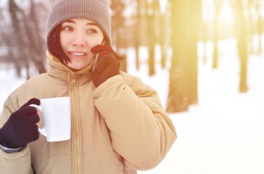 Oldukça çekici beyaz gözlü kız hipster kış Park portresi. Modern smartphone ve içecek kahve konuşuyor. Gençlik sokak moda. Açık havada yürüyüşler