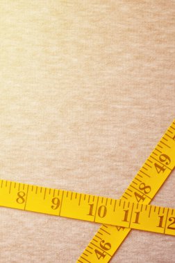 Cm veya inç şeklinde sayısal göstergeler ile sarı renk ölçüm bandı üzerinde gri bir örme kumaş yatıyor. Arka plan görüntüsü dikiş kıyafetler, insanlar için hakkında kim zayıflama