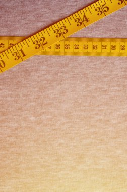 Cm veya inç şeklinde sayısal göstergeler ile sarı renk ölçüm bandı üzerinde gri bir örme kumaş yatıyor. Arka plan kavramı belirli vücut boyutları için dikiş ceketler