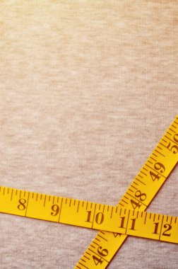 Cm veya inç şeklinde sayısal göstergeler ile sarı ölçüm bandı üzerinde gri bir örme kumaş yatıyor. Belirli vücut boyutları için dikiş spor giyim ile ilgili kavram sanayi