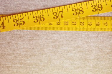 Cm veya inç şeklinde sayısal göstergeler ile sarı renk ölçüm bandı üzerinde gri bir örme kumaş yatıyor. Arka plan kavramı belirli vücut boyutları için dikiş ceketler