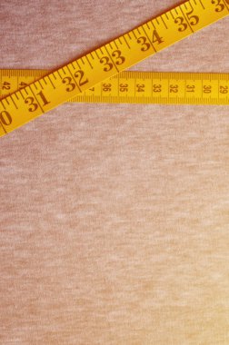 Cm veya inç şeklinde sayısal göstergeler ile sarı renk ölçüm bandı üzerinde gri bir örme kumaş yatıyor. Arka plan görüntüsü dikiş kıyafetler, insanlar için hakkında kim zayıflama