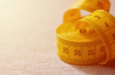 Cm veya inç şeklinde sayısal göstergeler ile sarı renk ölçüm bandı üzerinde gri bir örme kumaş yatıyor. Arka plan kavramı belirli vücut boyutları için dikiş ceketler