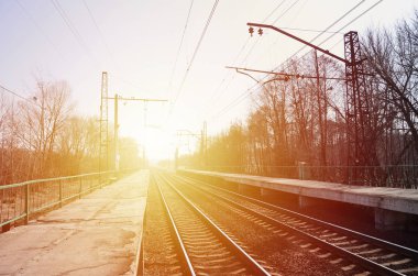 Bir tren istasyonu trenler güneşli bir günde bir çok ağaçlar ve tarlaları arasında bir kentsel yerleşim için beklediğiniz platformları ile. Demiryolu erken Bahar sezonu