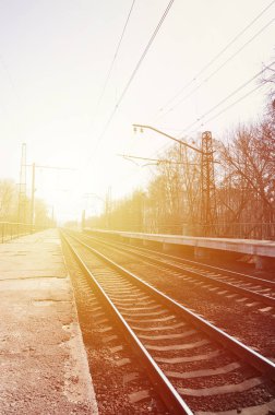 Bir tren istasyonu trenler güneşli bir günde bir çok ağaçlar ve tarlaları arasında bir kentsel yerleşim için beklediğiniz platformları ile. Demiryolu erken Bahar sezonu