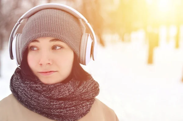 Oldukça çekici beyaz gözlü kız hipster kış park portresi. Kulaklıklar üzerinde müzik dinliyor. Gençlik sokak moda. Kış eğlence.