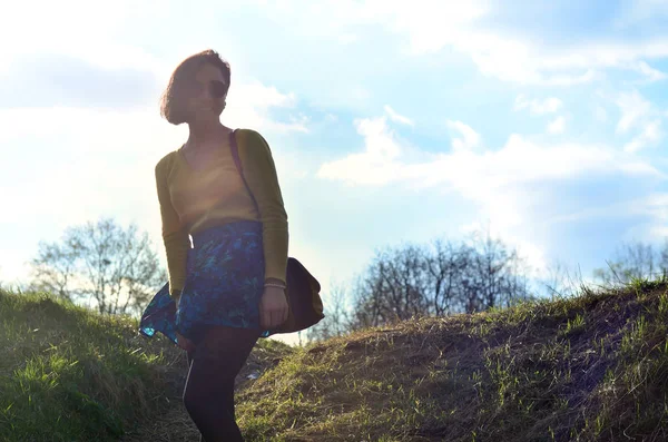 Bir çekici ve güzel esmer parlak sarı kazak ve yuvarlak siyah gözlük mutlu bahar alan yürür. Bir bahar güneşli gün boyunca neşeli bir esmer fotoğraf