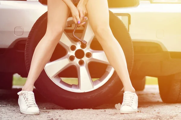 Genç ve seksi kız tekerlek anahtar ile hafif t-shirt ve mavi kot şort büyük ve gümüş araba tekerlek üzerinde oturuyor