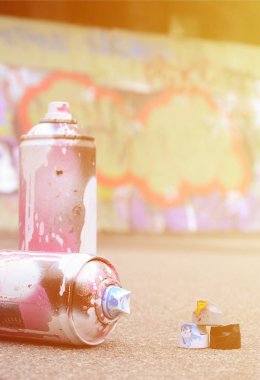 Pembe ve beyaz boya ve baskı altında boya püskürtme için kapaklar ile çeşitli kullanılan sprey kutular renkli grafiti çizimler boyalı duvarın yanında asfalt üzerinde yalan olduğunu