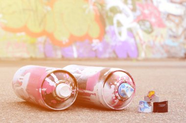 Pembe ve beyaz boya ve baskı altında boya püskürtme için kapaklar ile çeşitli kullanılan sprey kutular renkli grafiti çizimler boyalı duvarın yanında asfalt üzerinde yalan olduğunu