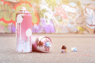 Pembe ve beyaz boya ve baskı altında boya püskürtme için kapaklar ile çeşitli kullanılan sprey kutular renkli grafiti çizimler boyalı duvarın yanında asfalt üzerinde yalan olduğunu