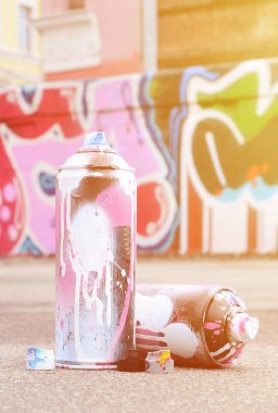 Pembe ve beyaz boya ve baskı altında boya püskürtme için kapaklar ile çeşitli kullanılan sprey kutular renkli grafiti çizimler boyalı duvarın yanında asfalt üzerinde yalan olduğunu
