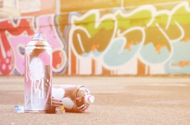 Pembe ve beyaz boya ve baskı altında boya püskürtme için kapaklar ile çeşitli kullanılan sprey kutular renkli grafiti çizimler boyalı duvarın yanında asfalt üzerinde yalan olduğunu