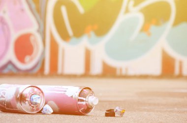 Pembe ve beyaz boya ve baskı altında boya püskürtme için kapaklar ile çeşitli kullanılan sprey kutular renkli grafiti çizimler boyalı duvarın yanında asfalt üzerinde yalan olduğunu