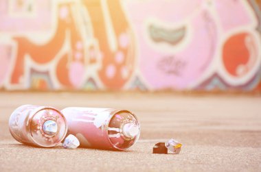 Pembe ve beyaz boya ve baskı altında boya püskürtme için kapaklar ile çeşitli kullanılan sprey kutular renkli grafiti çizimler boyalı duvarın yanında asfalt üzerinde yalan olduğunu