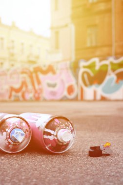 Pembe ve beyaz boya ve baskı altında boya püskürtme için kapaklar ile çeşitli kullanılan sprey kutular renkli grafiti çizimler boyalı duvarın yanında asfalt üzerinde yalan olduğunu