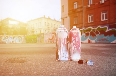 Pembe ve beyaz boya ve baskı altında boya püskürtme için kapaklar ile çeşitli kullanılan sprey kutular renkli grafiti çizimler boyalı duvarın yanında asfalt üzerinde yalan olduğunu