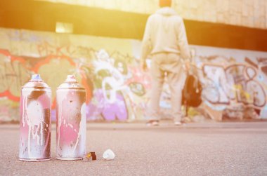 Birkaç kullanılan sprey pembe ve beyaz boya ile renkli grafiti bir boyalı duvar önünde duran adam asfaltta çizimler yalan