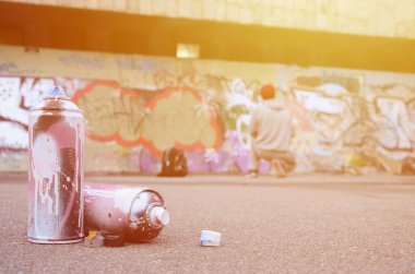 Birkaç kullanılan sprey pembe ve beyaz boya ile renkli grafiti bir boyalı duvar önünde duran adam asfaltta çizimler yalan